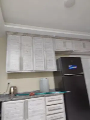 a kitchen with a black refrigerator and white cabinets at فيلا بيت الجبل in Ishtafaynā