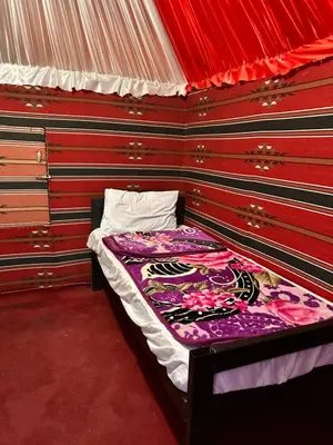 a small bed in a room with a red wall at Bedouin Camp&tour in Wadi Rum