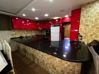 a kitchen with red cabinets and a black counter top at شقة للإجار في الجاردنز in ‘Urjān al Gharbīyah