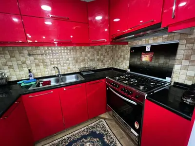 a red kitchen with a stove and a sink at شقة للإجار في الجاردنز in ‘Urjān al Gharbīyah