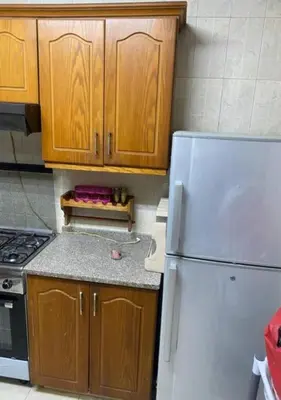 a kitchen with a white refrigerator and wooden cabinets at شقة مفروشة للايجار اسبوعي شهري سنوي طبربور in ‘Urjān al Gharbīyah