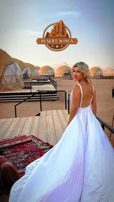 a woman in a white dress standing next to a table at RUM WINGS BUBBLES lUXURY CAMP in Wadi Rum