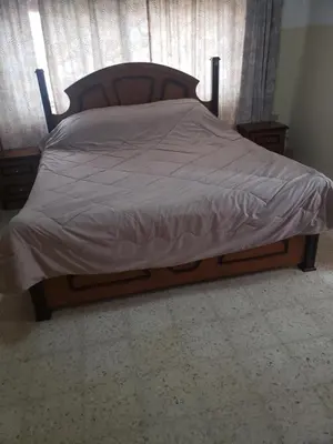 a bed with a wooden frame with a gray comforter at Al Otaibi in Umm Uthainah