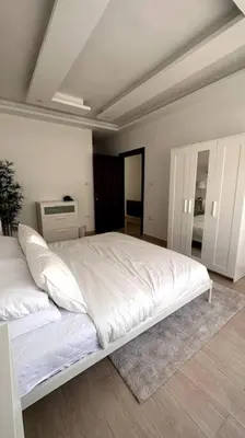 a bedroom with a large bed with white sheets at Modern & New 3-BR Entire Apt - Prime Location! in Rujm ash Sharāʼirah