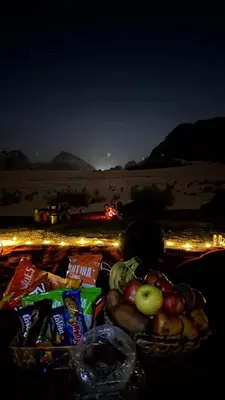 a basket of apples and chips on a beach at night at Camp star road safari in Wadi Rum