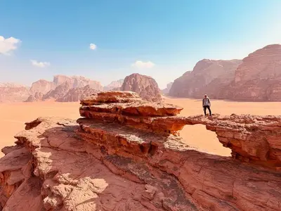 a man standing on a cliff in the desert at Wadi Rum Bedouin Story Camp & Tours in Wadi Rum