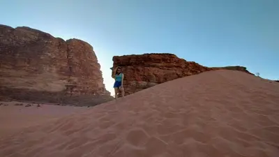 a woman standing on top of a mound of sand in the desert at Dream Bedouin Life Camp Wadi Rum in Disah