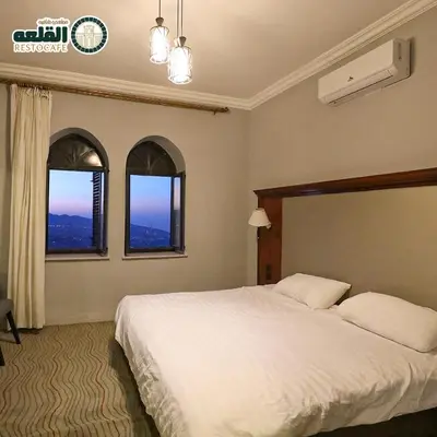 a bedroom with a large white bed with two windows at Alqalah Restotel فندق ومطعم القلعة in Kerak