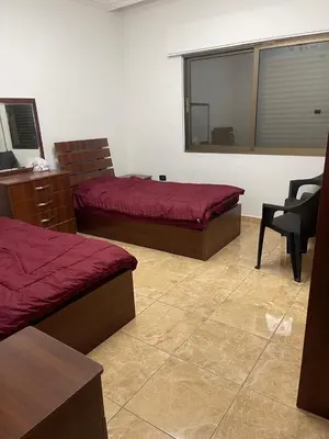 a bedroom with two beds and a chair and a window at Samar Home in Amman
