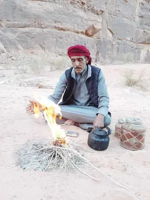 a man sitting on the ground in front of a fire at Ahmad and Fatima's Traditional Bedouin Camp in Wadi Rum