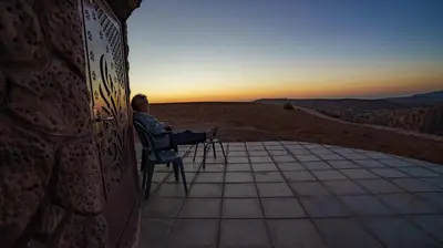 a man sitting in a chair watching the sunset at Al -Nawatef Eco Lodge- Dana Nature Reserve in Dana