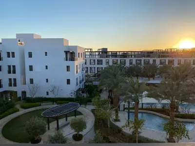 a view of a building with a pool and palm trees at Lovely 2-Bedroom with pool in the heart of Aqaba in Aqaba