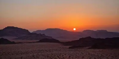 a sunset in the desert with mountains in the background at Ayman camp in Wadi Rum