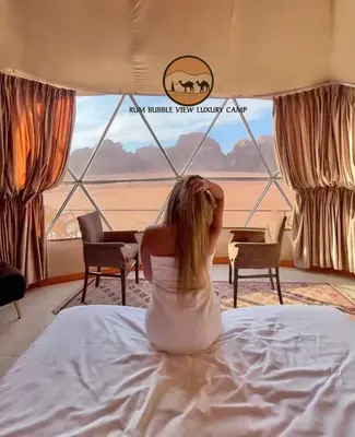 a woman sitting on a bed looking out a window at RUM BUBBLES VIEW lUXURY CAMP in Wadi Rum