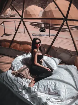 a woman sitting on a bed in a tent at RUM MARS lUXURY SANDS BUBBLE CAMP in Wadi Rum