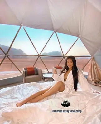 a woman sitting on a bed in a tent at RUM MARS lUXURY SANDS BUBBLE CAMP in Wadi Rum