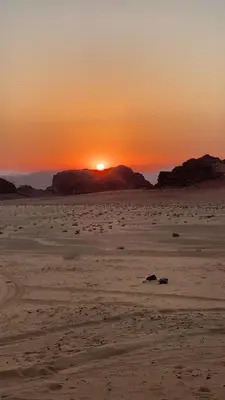 a sunset on a beach with the sun setting in the distance at Desert Magic Camp in Wadi Rum