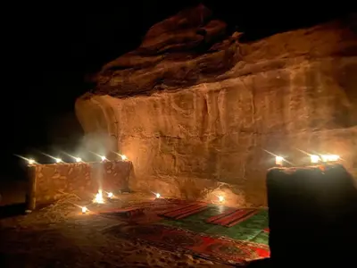 a room with candles and a stone wall at night at Desert Magic Camp in Wadi Rum