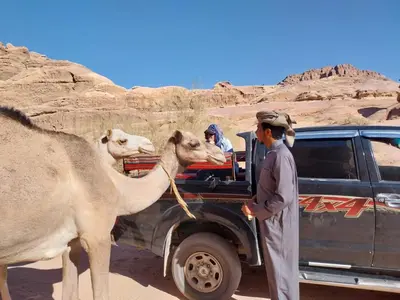 a man with a camel standing next to a truck at Wadi Rum Red Desert in Wadi Rum