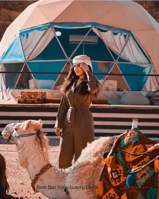 a woman is standing next to a camel at RUM STAR VIEW BUBBLES lUXURY CAMP in Wadi Rum