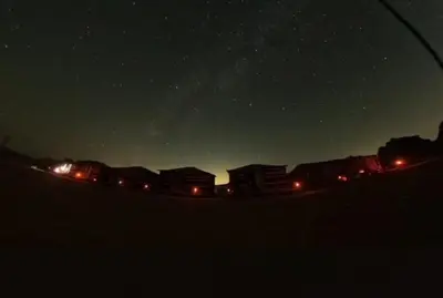a starry night with houses and lights in the distance at Wadi rum camp with tour in Wadi Rum