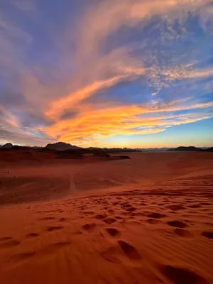 a sunset in the desert with footprints in the sand at Princess Camp in Wadi Rum