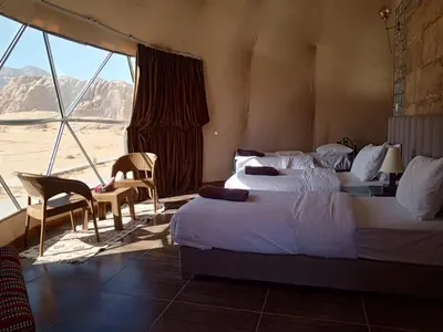 a bedroom with two beds and a view of the desert at Amber Luxury Camp in Maḩaţţat Dīsah