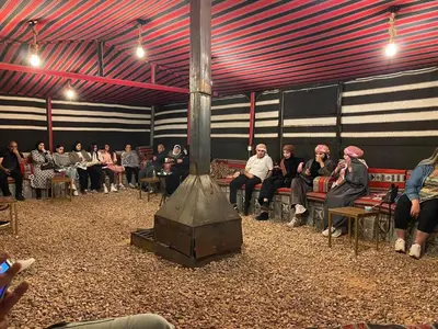 a group of people sitting in a room with a fireplace at Amber Luxury Camp in Maḩaţţat Dīsah