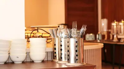 a container of utensils on a counter with white cups at Aysel Hotel in Aqaba