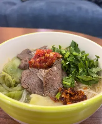 a bowl of soup with meat and greens on a table at \u9f99\u95e8\u5ba2\u6808 in Amman