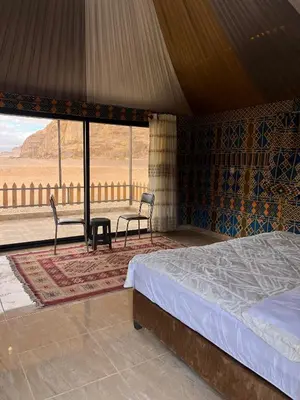 a bed and two chairs in a room with a view at Rum STAR LUXURY Camp &JEEP Tours in Wadi Rum