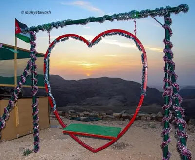 a heart shaped swing with the sunset in the background at Wadi Ghowair View Camp in Al Khuraybah