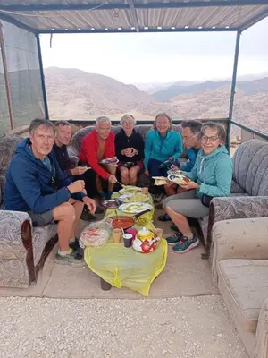 a group of people sitting around a table with food at Wadi Ghowair View Camp in Al Khuraybah