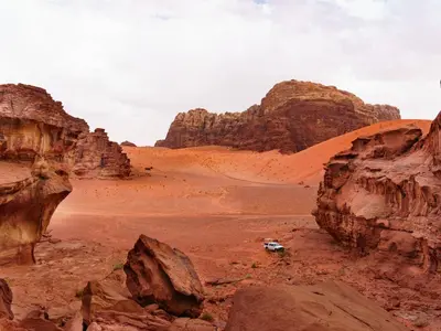 a car in the desert with rocks and a mountain at Wadi Rum 5-hour tour with sunset or morning, overnight stay with two meals and a Bedouin tent with a private bathroom Prices are for two people in Wadi Rum