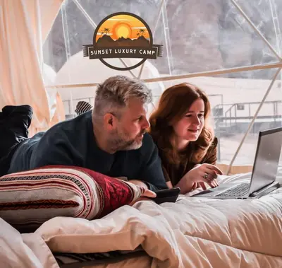 a man and a woman laying on a bed with a laptop at RUM SUNSET BUBBLES lUXURY CAMP in Wadi Rum