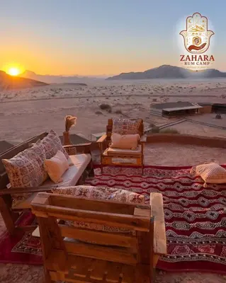 a couch and chairs in the desert with the sunset at Zahara rum camp & Boutique Resort in Disah
