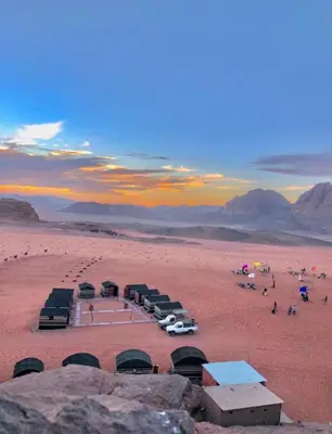 a group of tents in the desert with a sunset at Wadi Rum sleeping in the desert in Wadi Rum