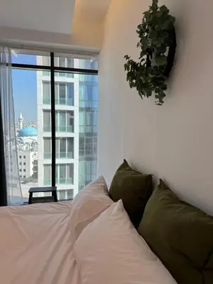 a bedroom with a white bed and a plant on the wall at DAMAC City View Penthouse in Amman