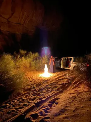 a woman standing next to a fire in the desert at night at Green Desert in Wadi Rum