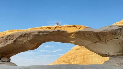 a person standing on top of an arch in the desert at WADI RUM STAR LOTE LUXURY CAMp & BUBBLES ROOM in Wadi Rum