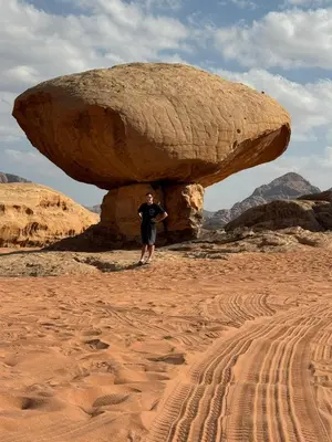 a man standing under a large rock in the desert at Wadi Rum murahf camp in Wadi Rum