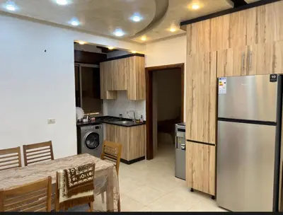 a kitchen with a table and a stainless steel refrigerator at شقه مفروشة ذات اطلالة جميلة ومكان هادئ in Irbid