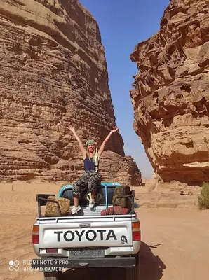 a woman sitting on the back of a truck in the desert at Rum gate camp Fares in Disah