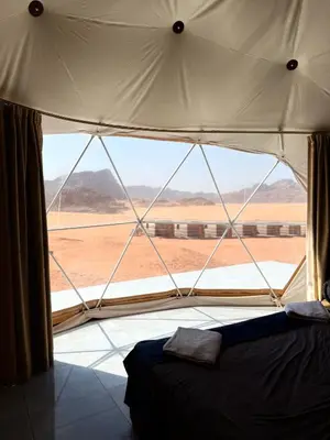 a bedroom with a large window with a view of the desert at Ayla Rum Luxury Camp in Wadi Rum