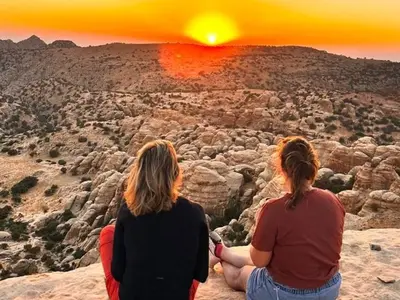 two women sitting on a cliff watching the sunset at Jordan trail from dana to petra in Dana