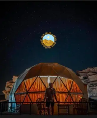 a man standing in front of a yurt at night at RUM BUBBLES VIEW MARS lUXURY CAMP in Wadi Rum