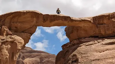 a man standing on top of an arch in a canyon at Crown Luxury Camp in Wadi Rum