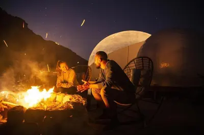 two people sitting around a fire next to a tent at Crown Luxury Camp in Wadi Rum