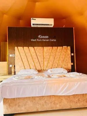 a bed with a wooden headboard in a room at Wadi Rum Kenan Camp in Wadi Rum