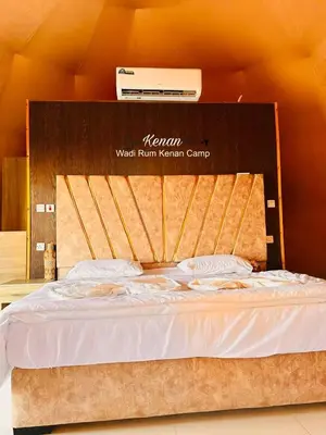 a bed with a wooden headboard with avertisement at Wadi Rum Kenan Camp in Wadi Rum